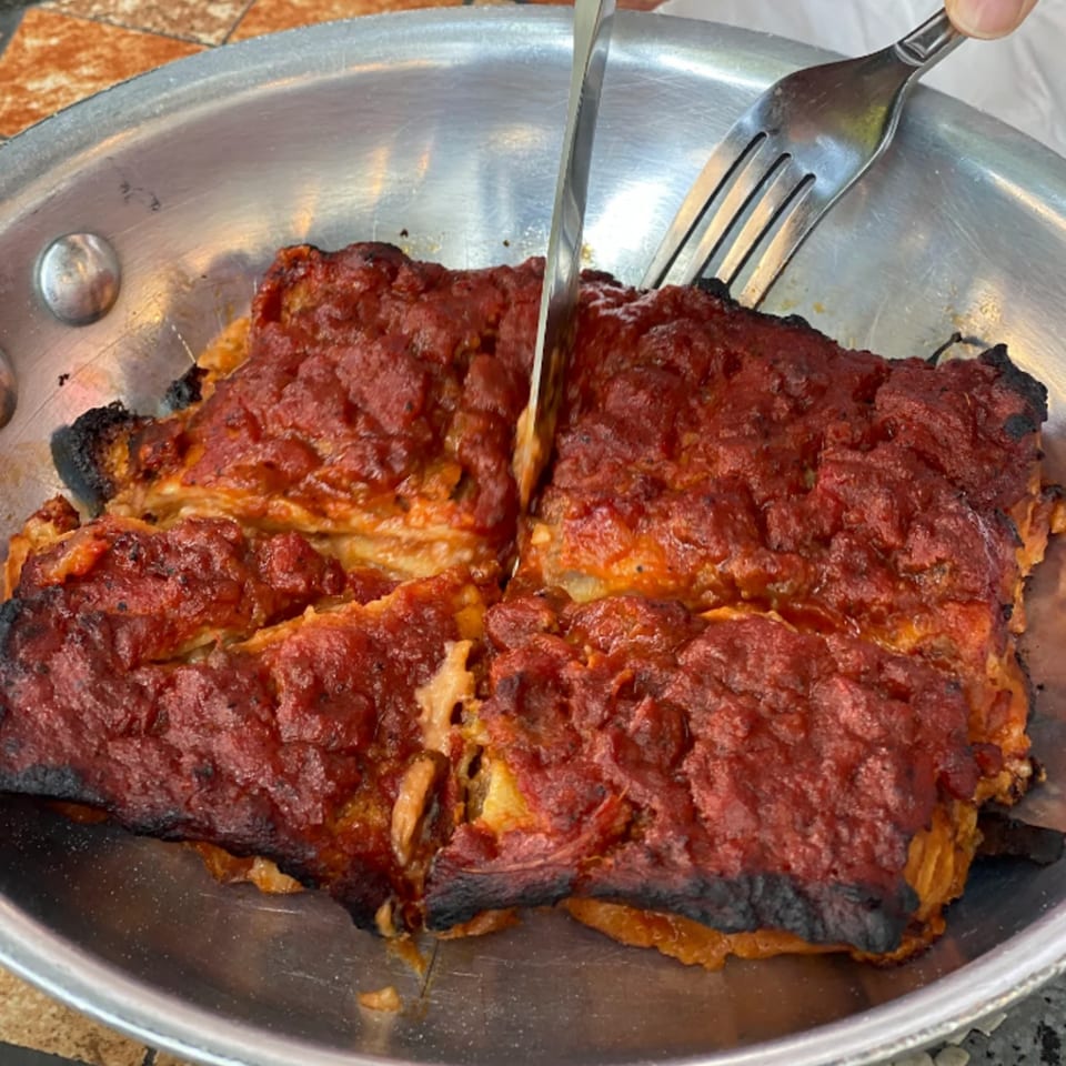 A knife and fork cutting into a large, rectangular portion of Marcella's Lasagneria's lasagna.