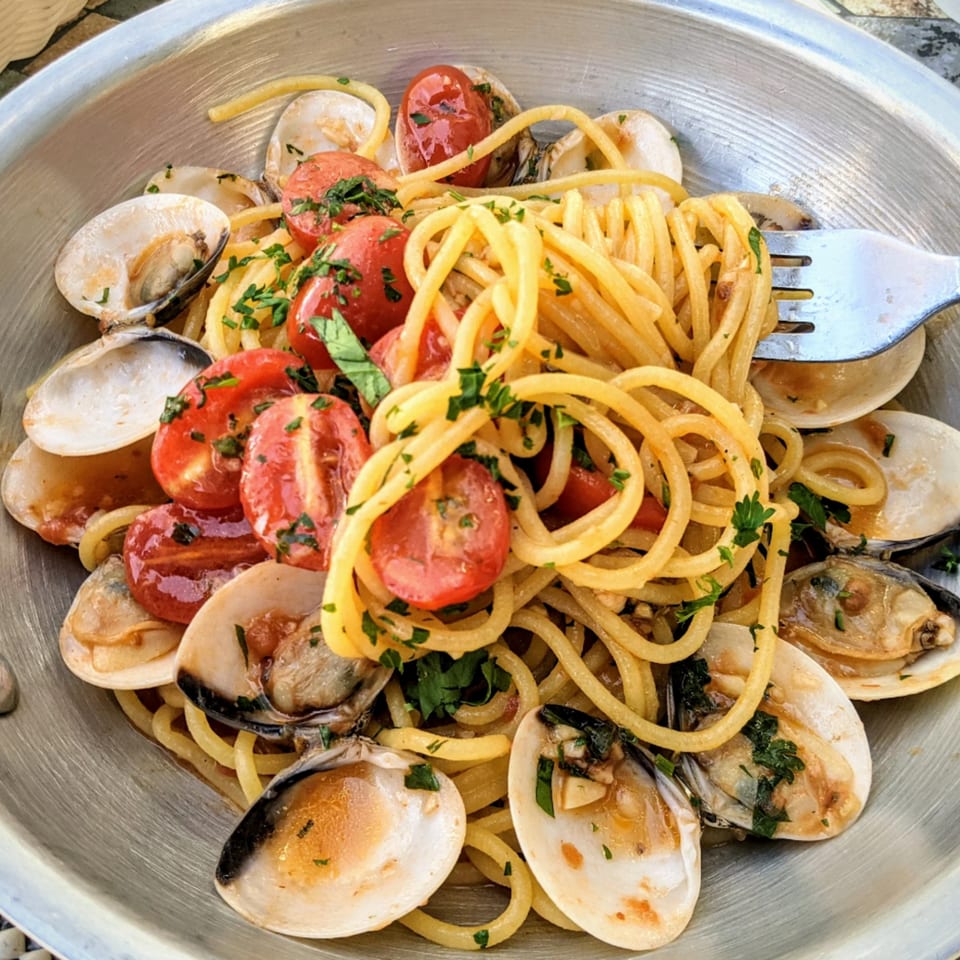 Spaghetti alle vongole with cherry tomatoes and parsley in a metal pan, with a fork.