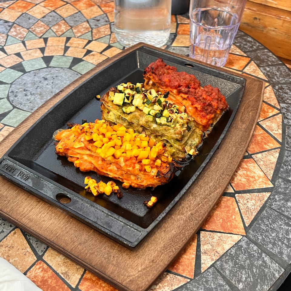 Three colorful lasagna portions, red, green, and orange, on a black cast iron plate.