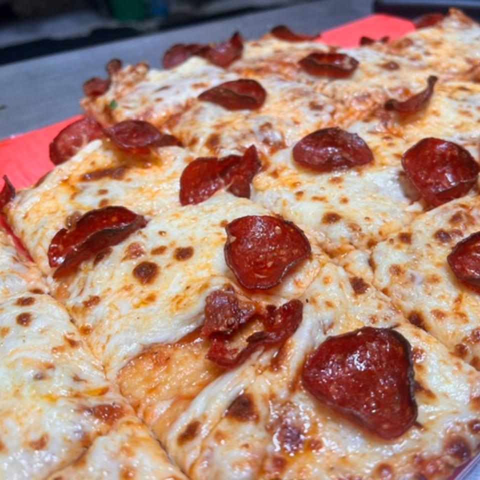 Close-up of a freshly baked pepperoni pizza, cut into squares, with melted cheese and crispy pepperoni.