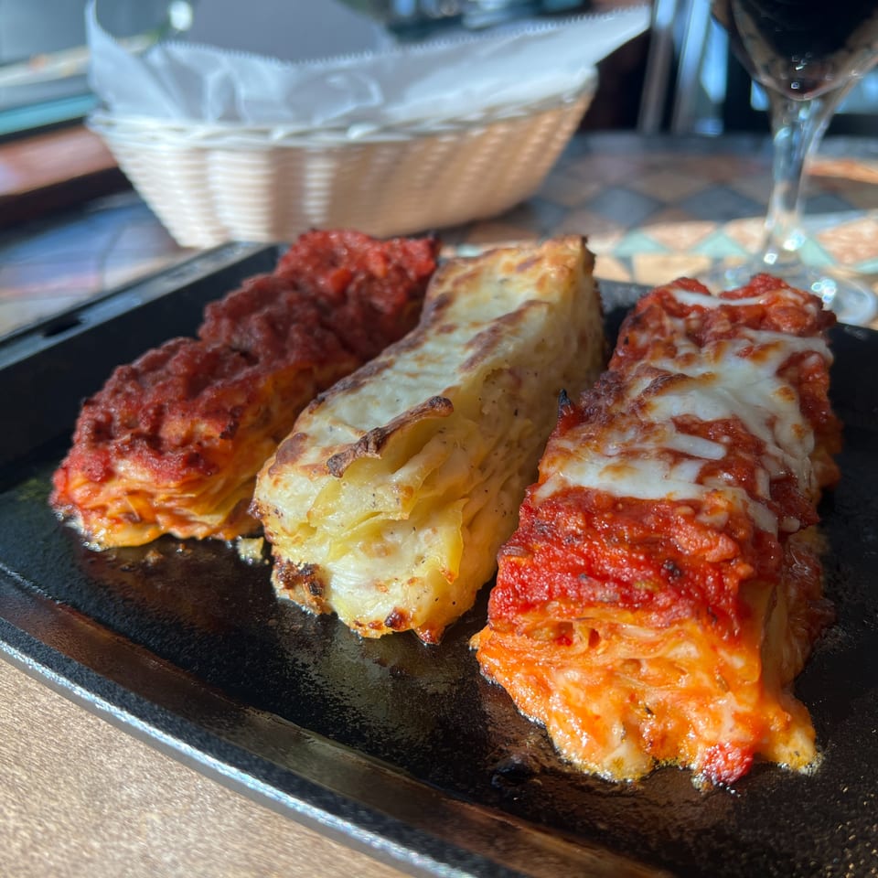 Three servings of Marcella's lasagna, two with red sauce and one with white sauce, on a black plate.