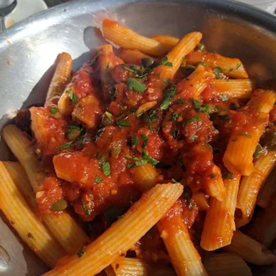 Penne pasta with red tomato sauce and fresh parsley in a metal bowl.